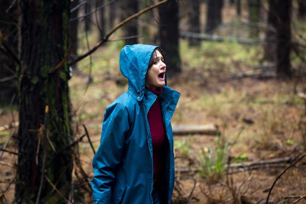 Actress Emily Mortimer screaming in a woodland wearing a blue anorak, from the film Relic.